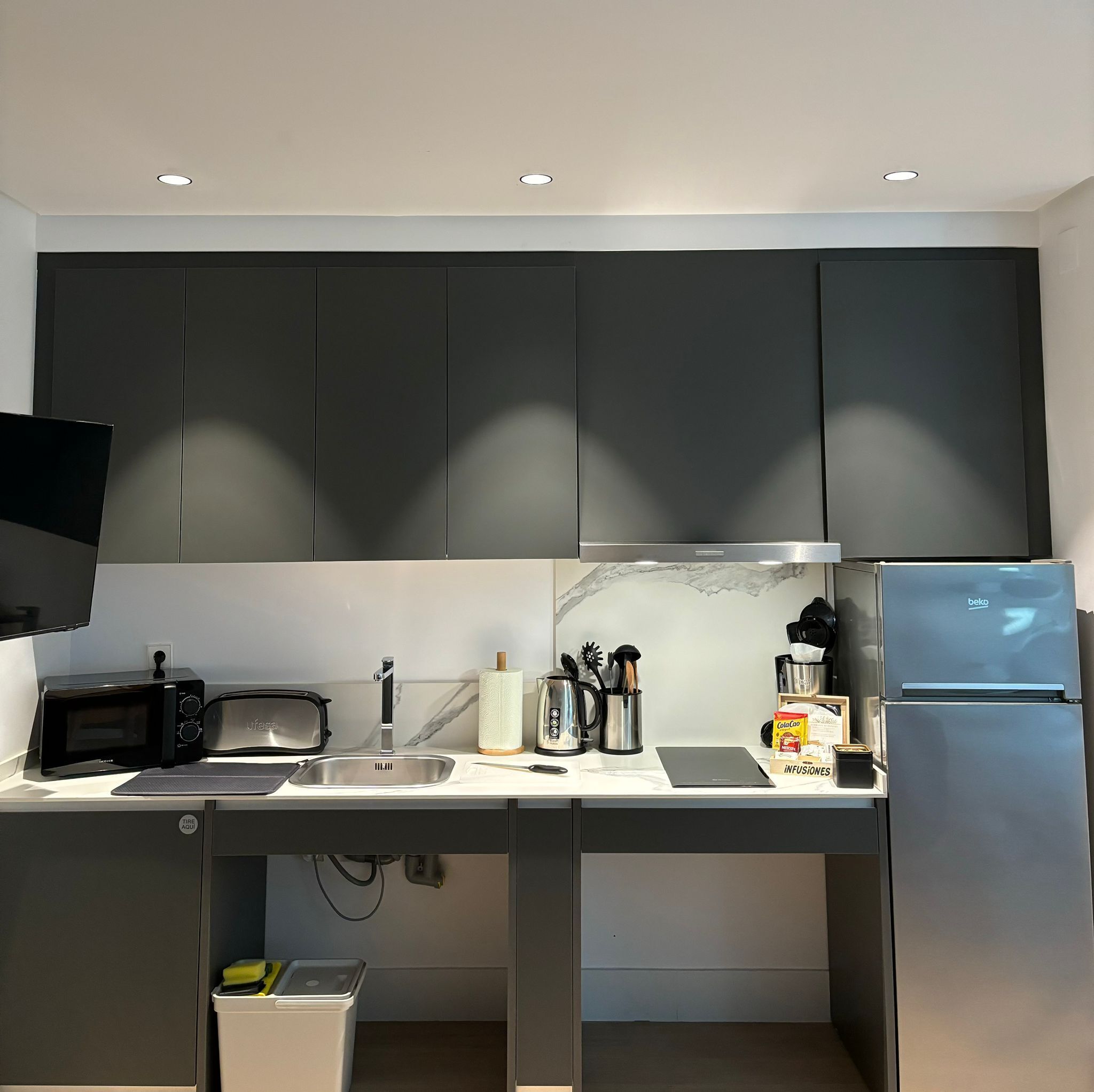 A modern kitchen with dark cabinets, a built-in microwave, a sink, and a refrigerator.