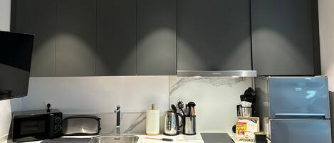 A modern kitchen with dark cabinets, a built-in microwave, a sink, and a refrigerator.