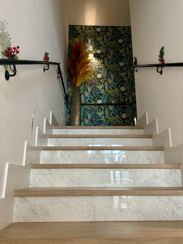 Eine Treppe mit Marmorstufen und Holengeländern, die zu einem Raum mit Blumenmuster-Tapete führt.