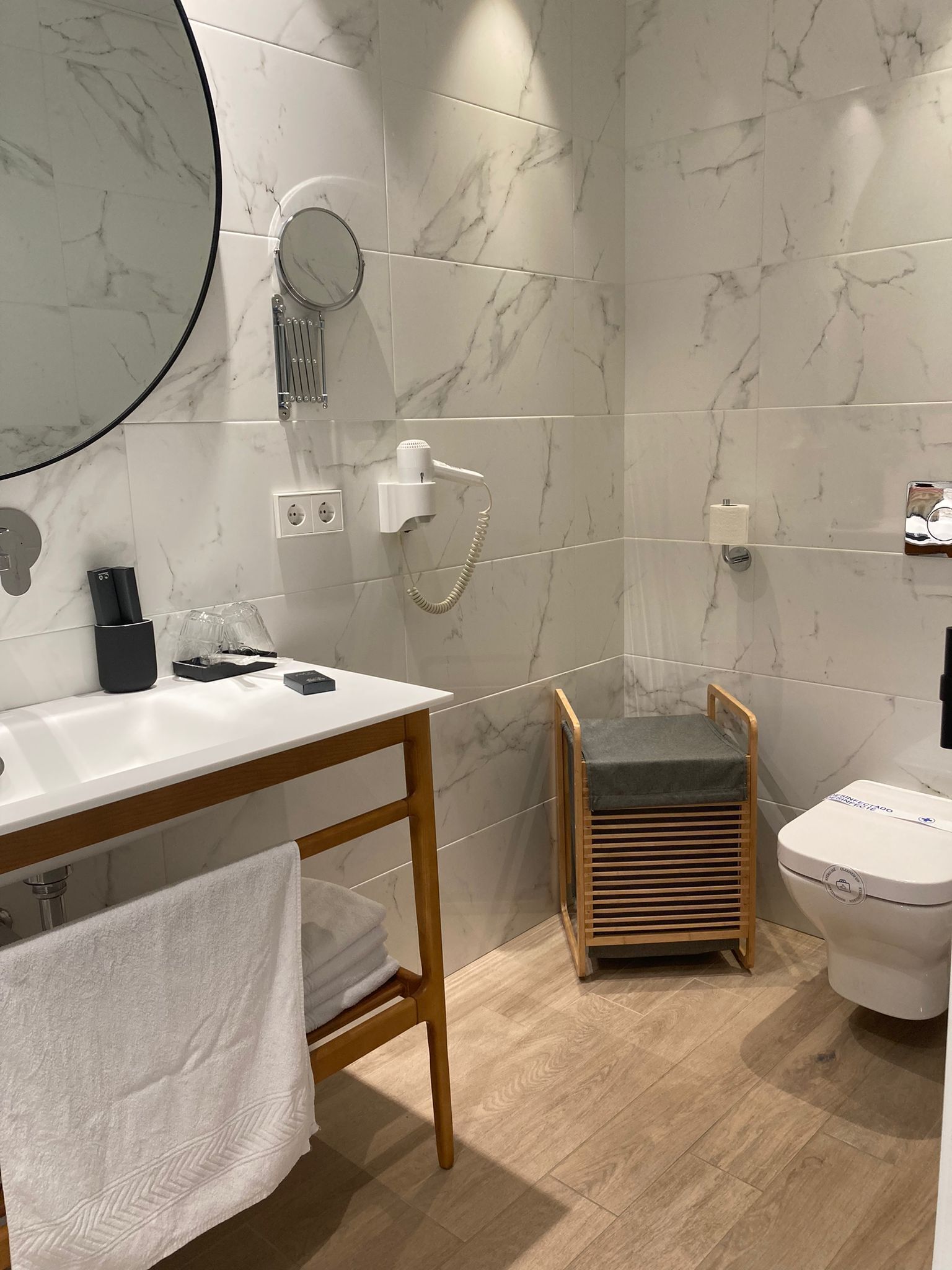 Un baño moderno con pared de mármol, tocador de madera, asiento de ducha y un inodoro.