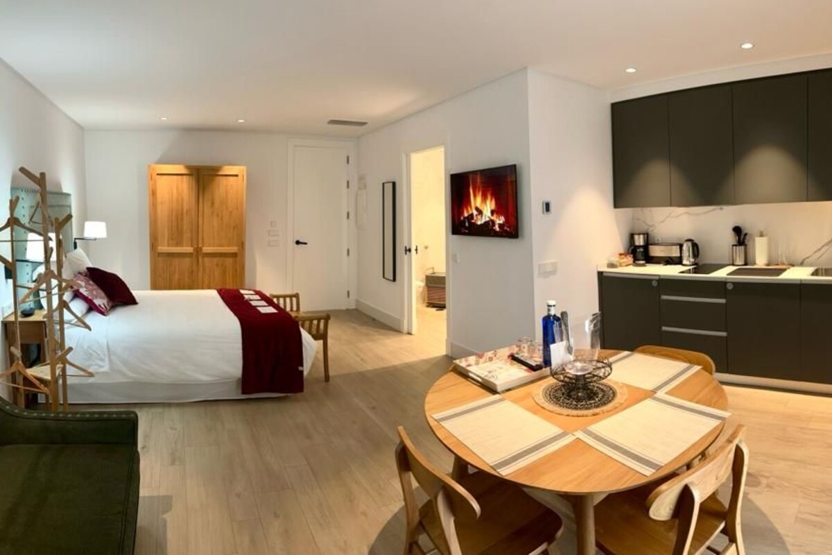 A modern hotel room with a bed, a dining table, and a kitchen area.