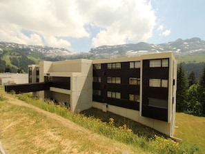 Situated in a natural setting, this building offers a contemporary design with multiple windows and a pathway leading to its entrance.