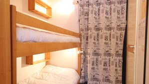 Une chambre avec un lit superposé, un rideau à motifs et une étagère en bois.