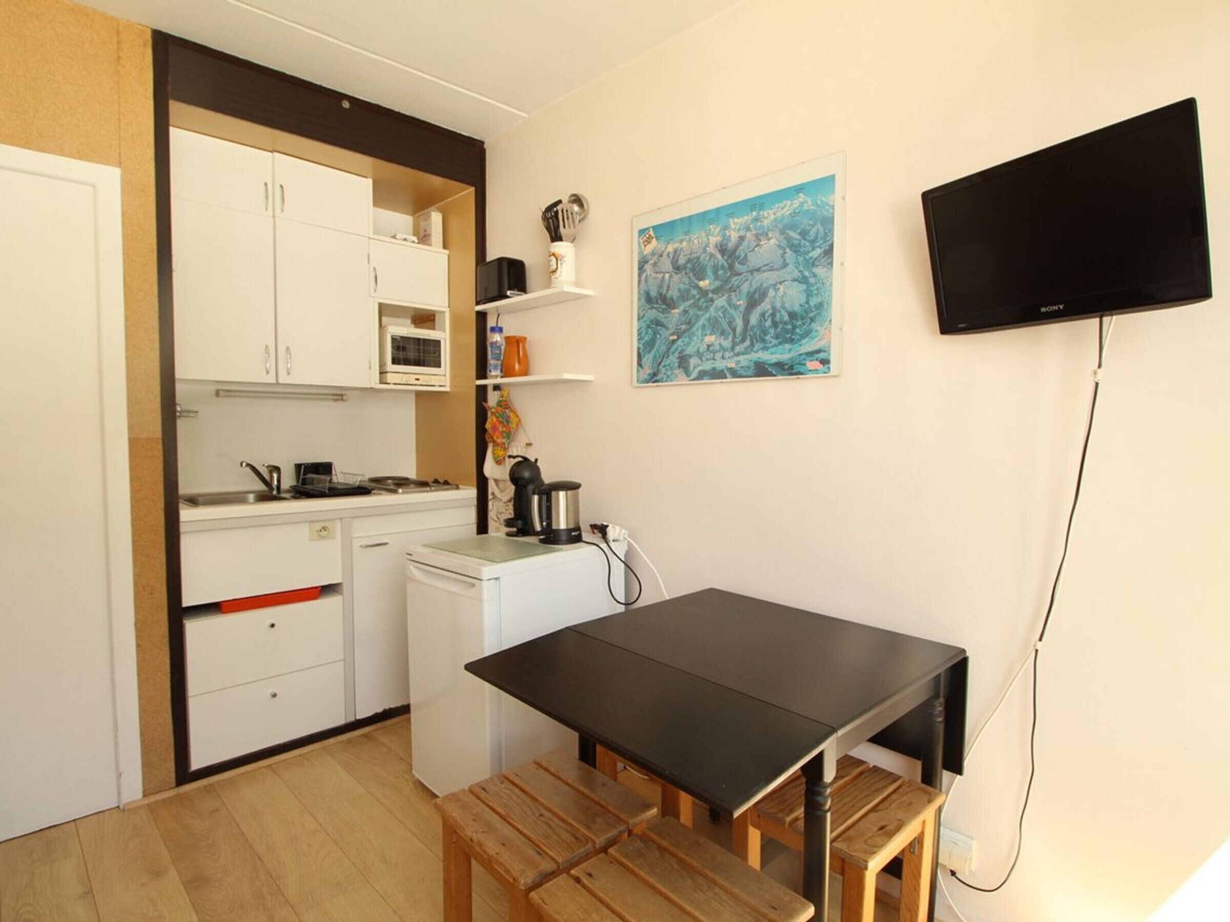 Een kleine keuken met witte kastjes, een magnetron, een koffiezetapparaat en een houten tafel met bankjes.