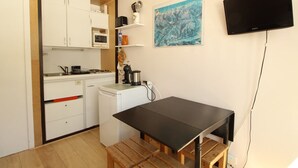 Une cuisine compacte avec des meubles blancs, un four à micro-ondes, une machine à café et une table en bois avec des bancs.