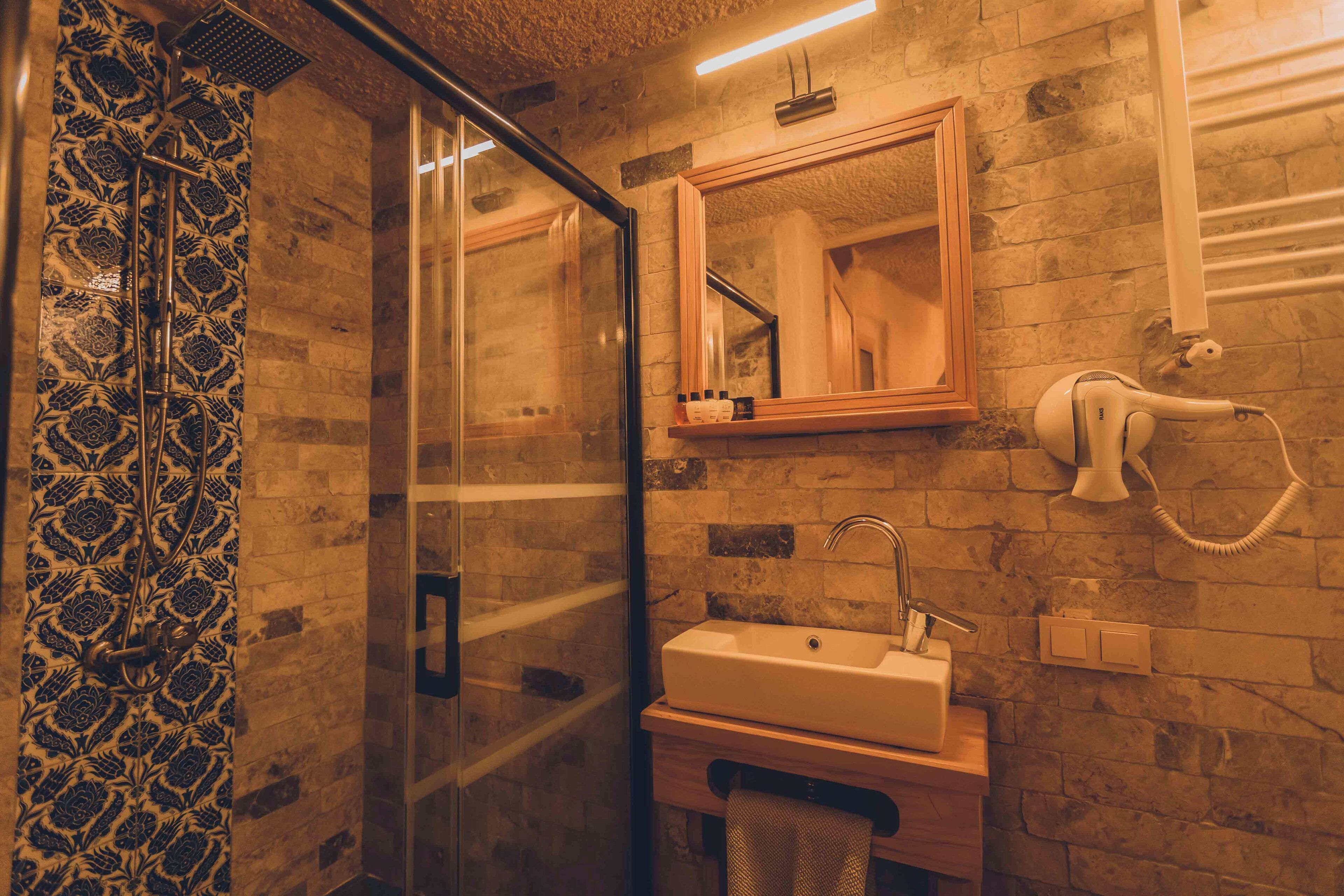 A bathroom with a glass shower enclosure, a sink, a mirror, and a hairdryer mounted on the wall.