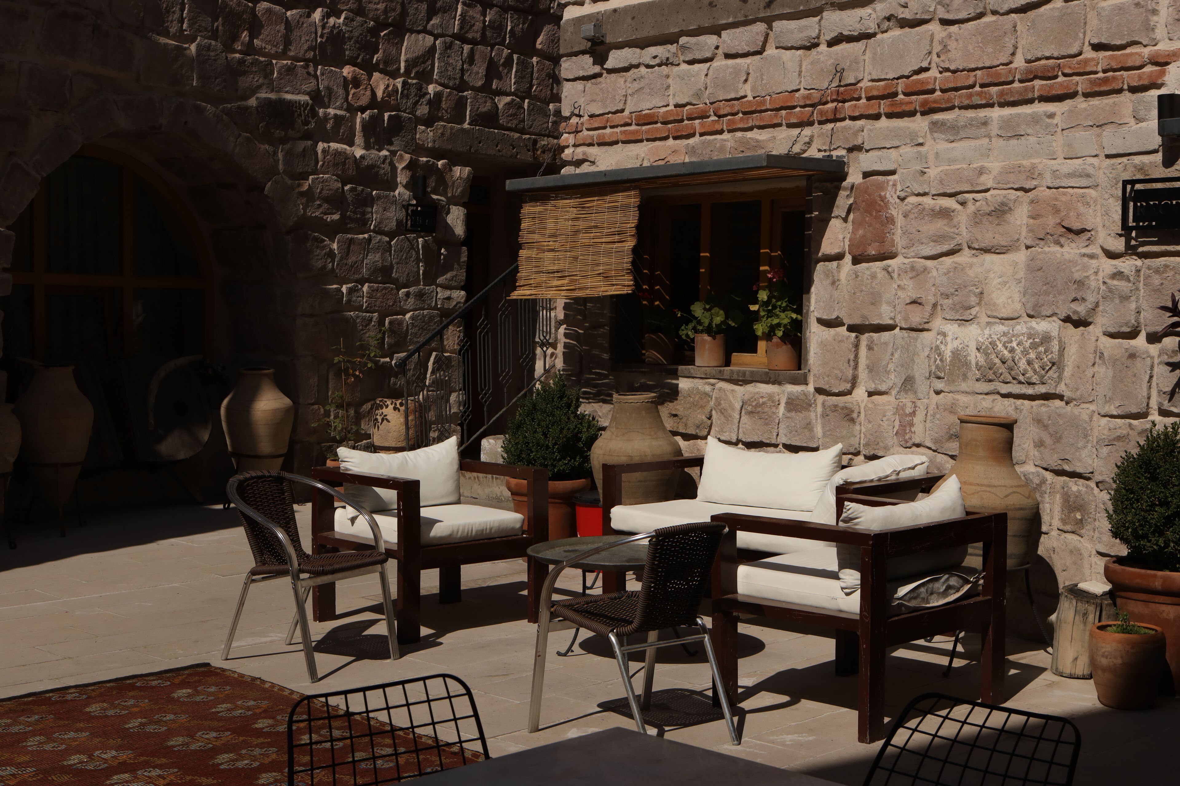 An outdoor seating area with wicker chairs and white cushions, stone walls, and potted plants.