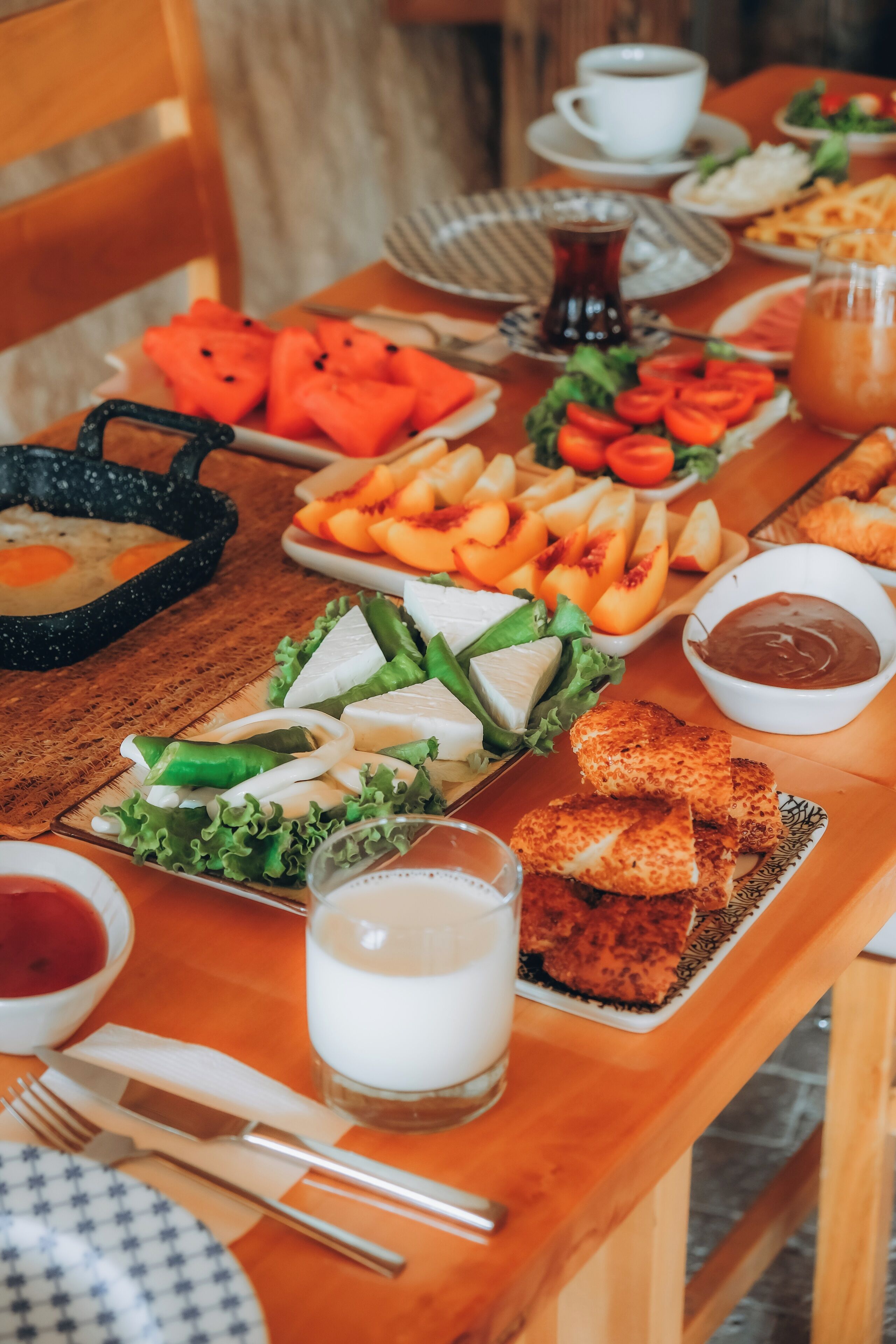 A wooden dining table with various dishes including eggs, fruits, and bread.