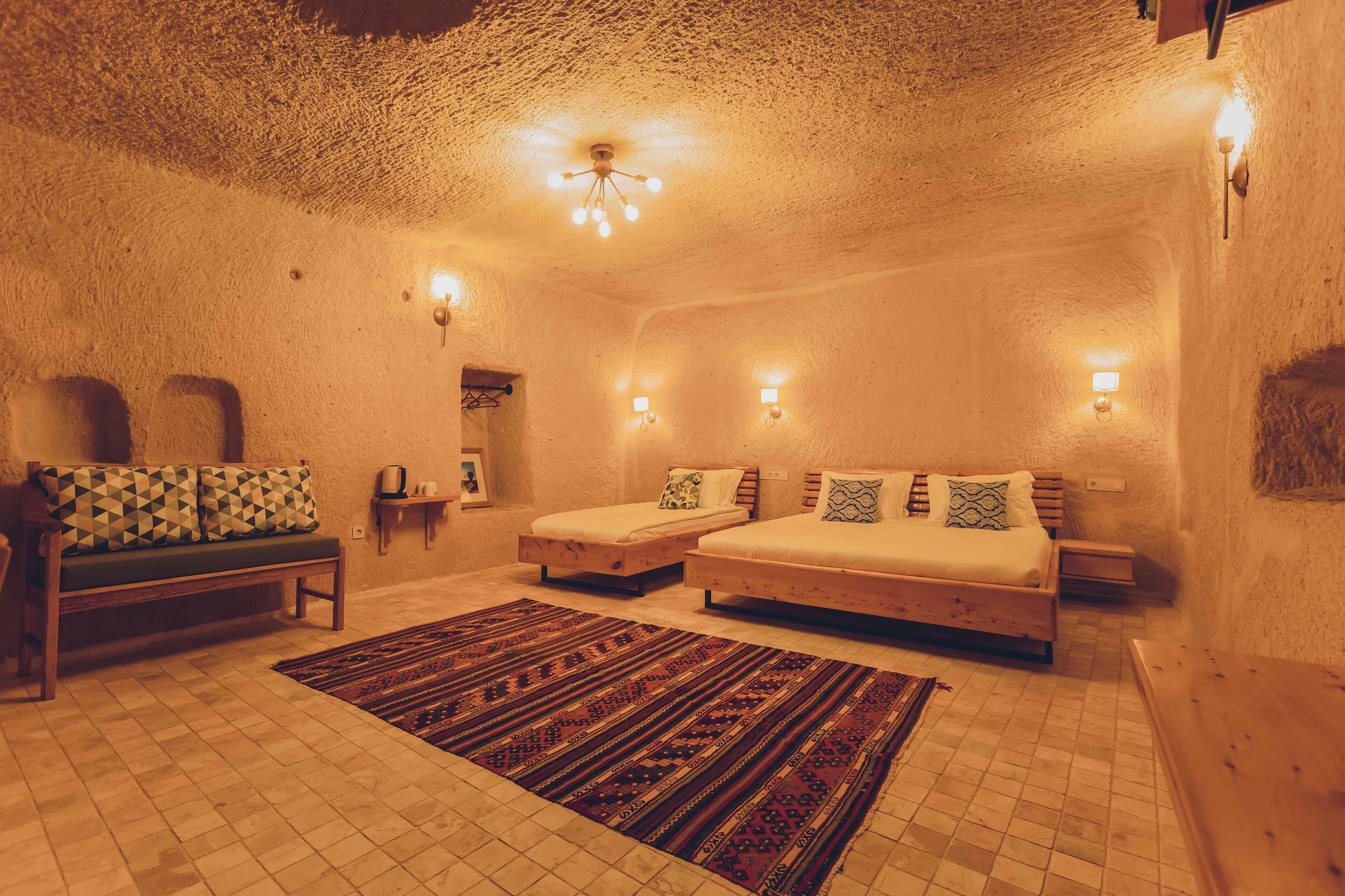 Une chambre confortable avec un grand lit, un plus petit lit, un banc et un tapis à motifs.