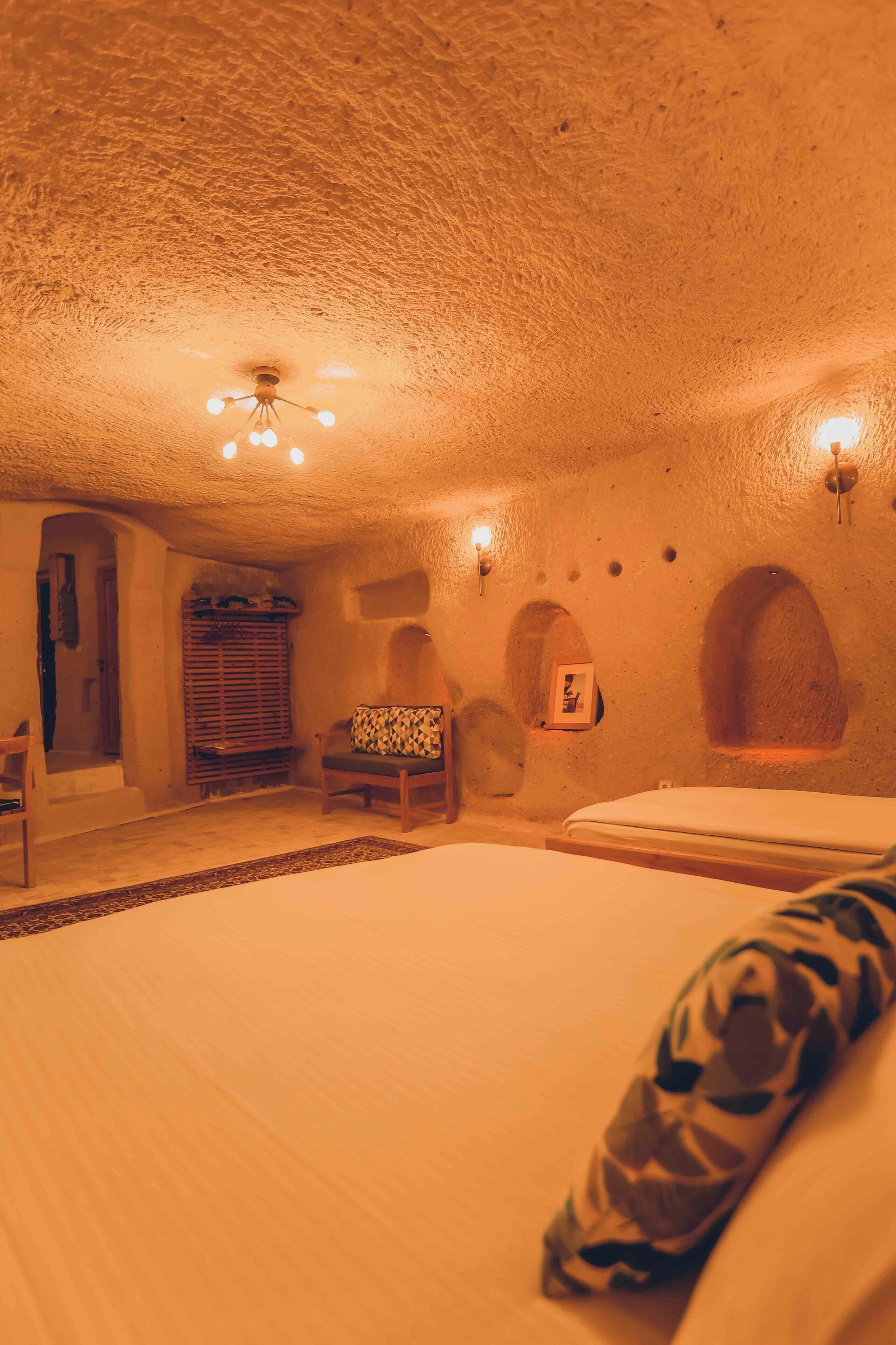 A cozy room with a bed, a chair, a small table, and a wall-mounted shelf.