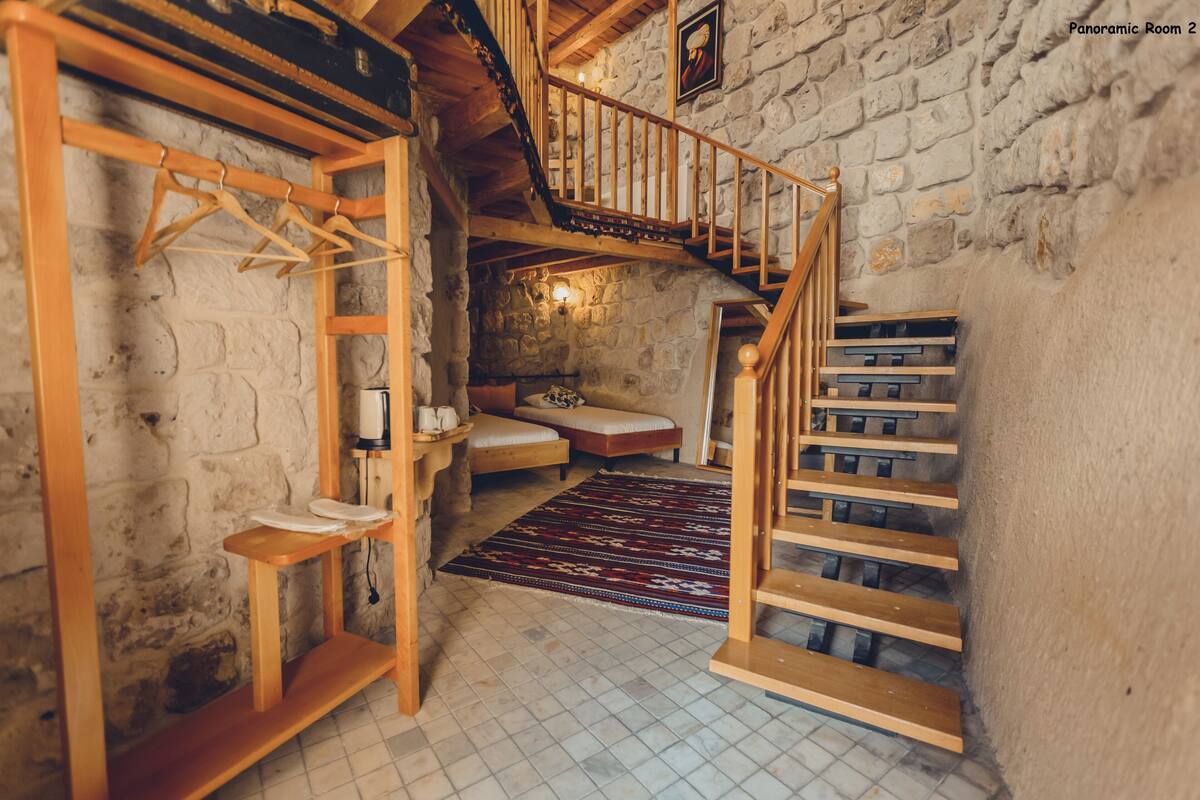 A rustic room with a wooden staircase, a stone wall, and a hanging clothes rack.