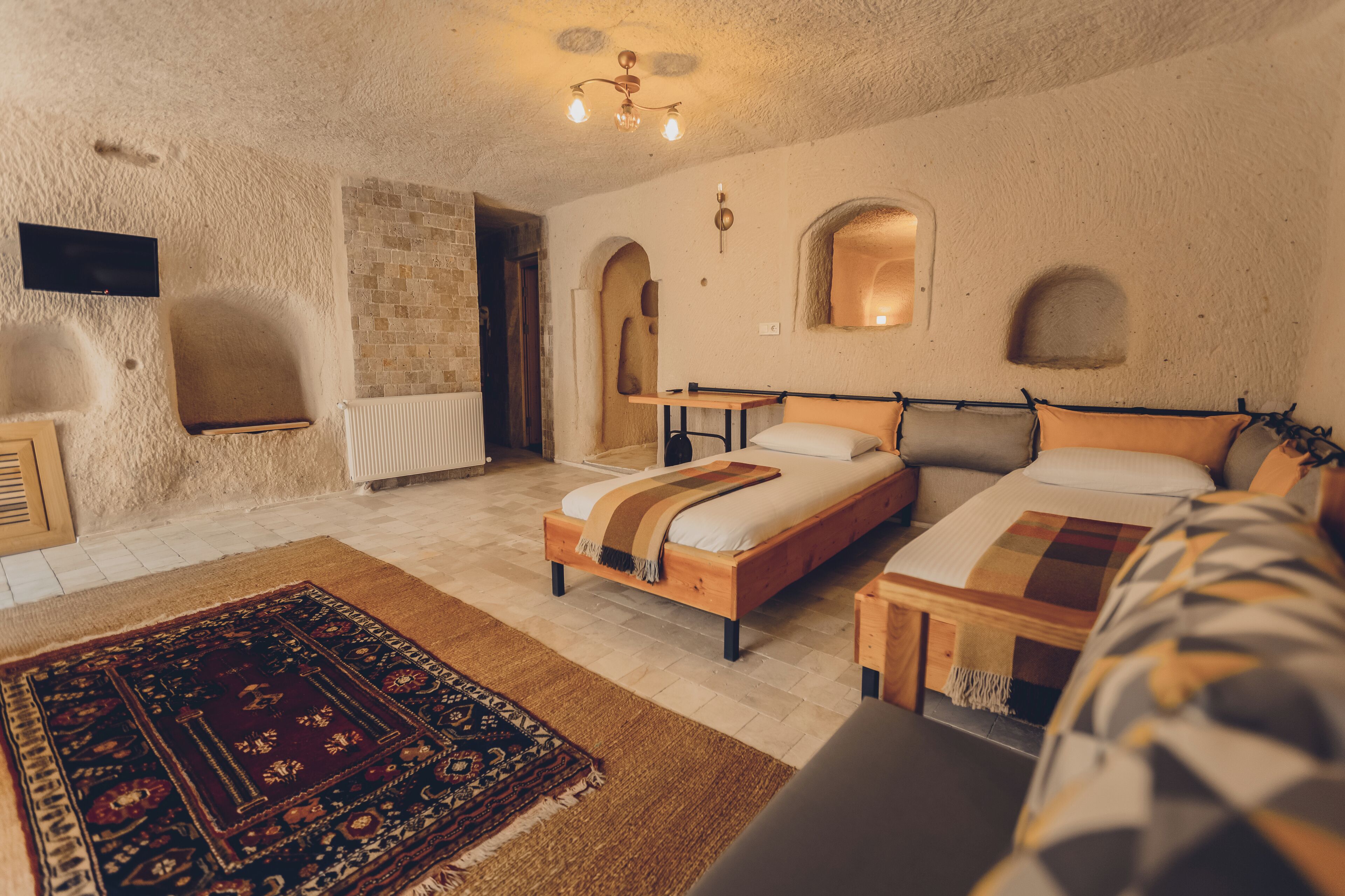 A cozy bedroom with a large bed, a smaller bed, a wooden nightstand, a TV, and a patterned rug.