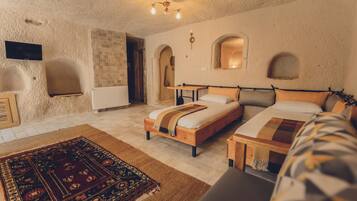 A cozy bedroom with a large bed, a smaller bed, a wooden nightstand, a TV, and a patterned rug.