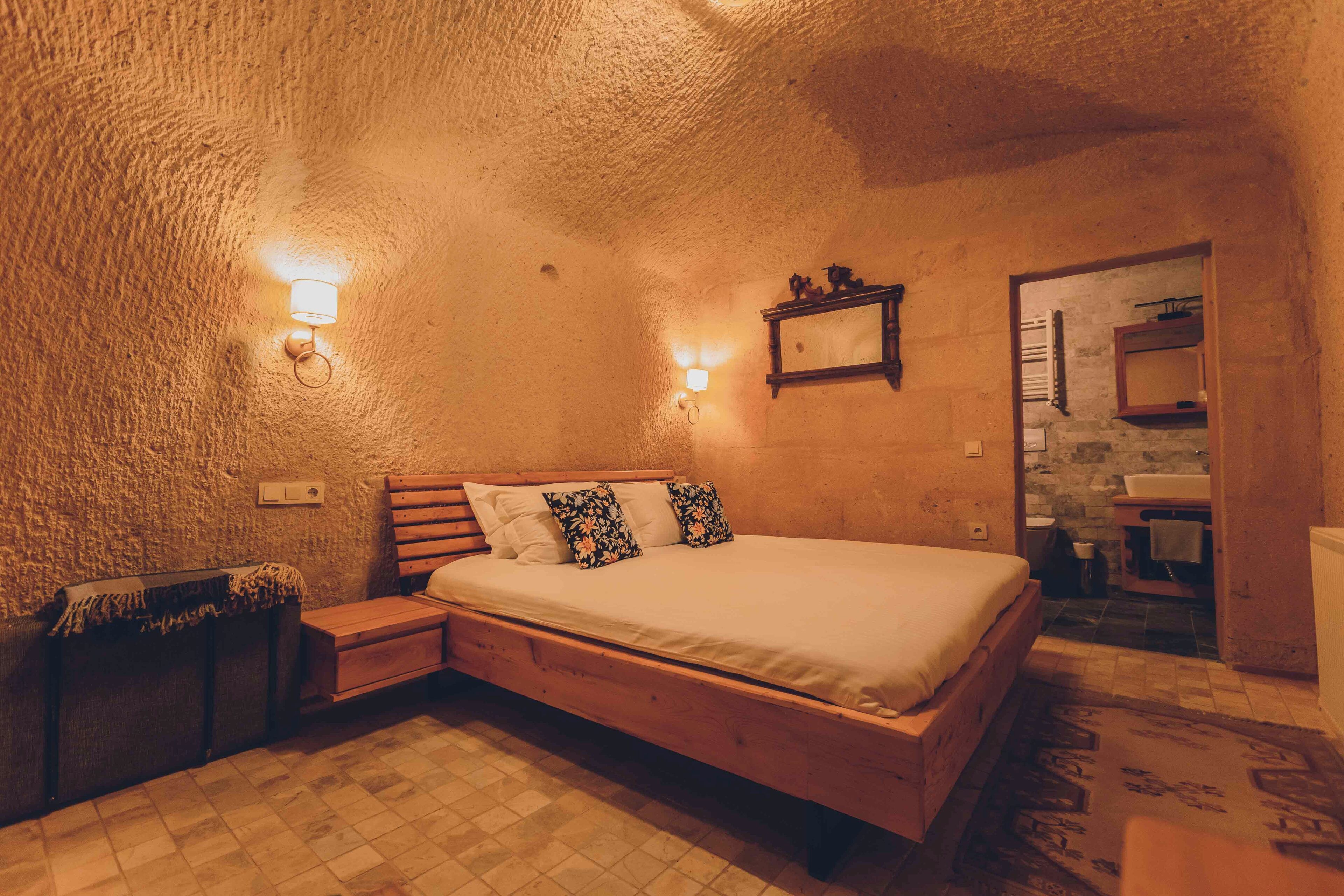 Ein gemütliches Schlafzimmer mit einem hölzernen Bett, einem Nachttisch, einem an der Wand befestigten Regal und einem durchgehenden Türspalt sichtbaren Badezimmer.