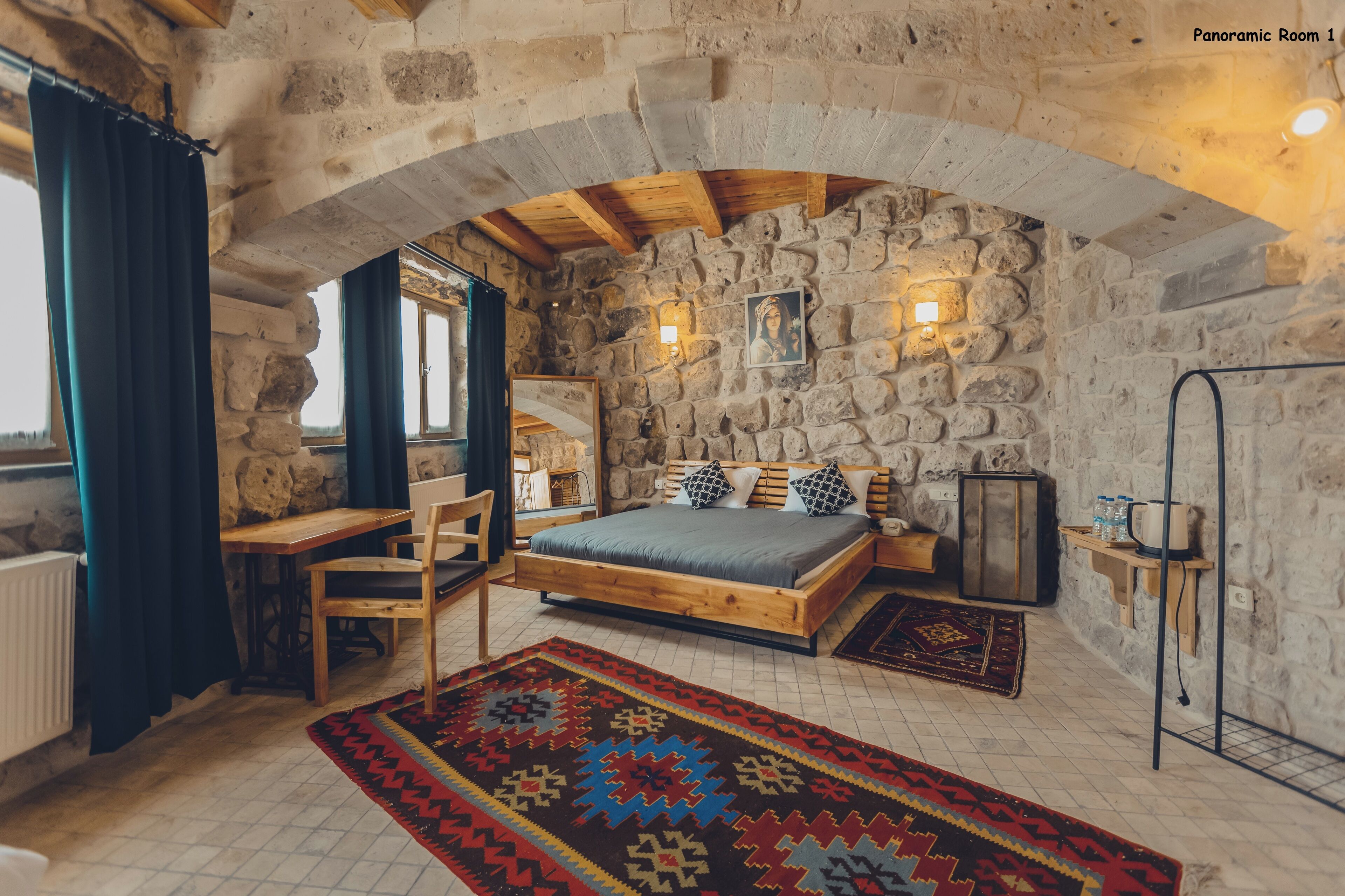 A rustic bedroom with a stone wall, wooden bed, and a view of the outdoors.