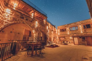 Une cour bordée de murs en pierre, une table en bois avec des chaises et un escalier menant à un niveau supérieur.