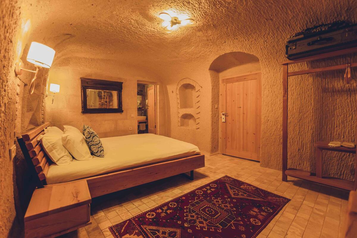 A bedroom with a wooden bed, a patterned rug, a wardrobe, and a small window.