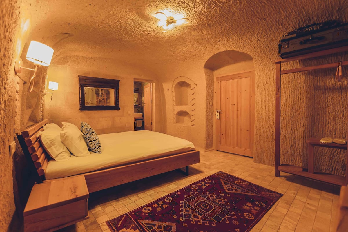 Un dormitorio con una cama de madera, una alfombra estampada, un armario y una ventana pequeña.