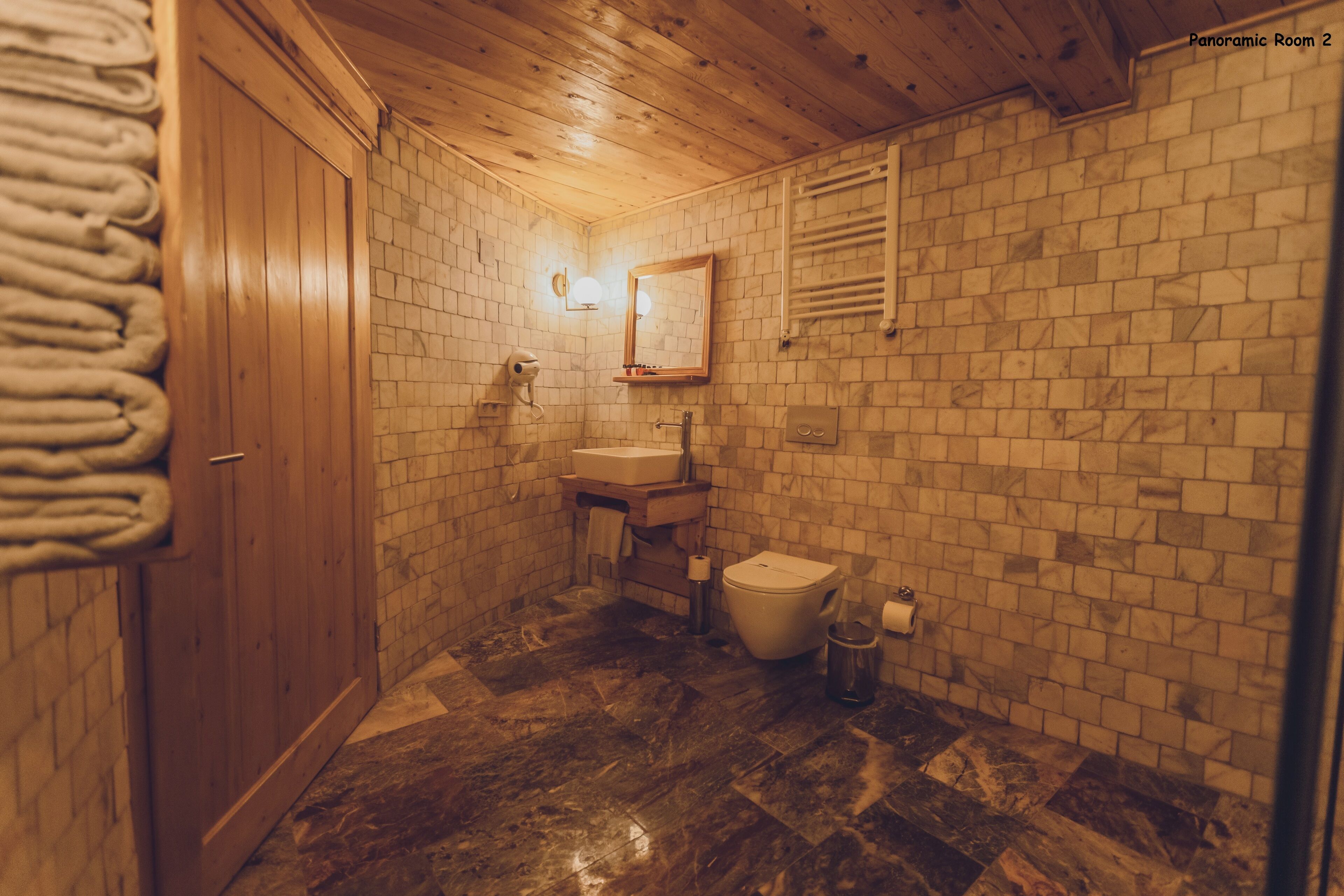 A bathroom with a wooden ceiling, a tiled wall, a sink, a toilet, and a towel rack.