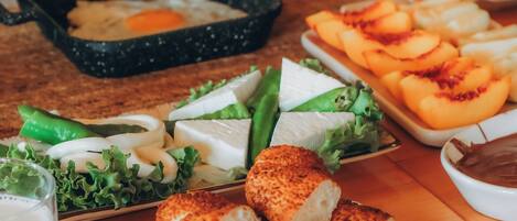 Une table en bois sur laquelle on trouve divers aliments, notamment une assiette de fromage, un bol de soupe et un plateau de fruits coupés.