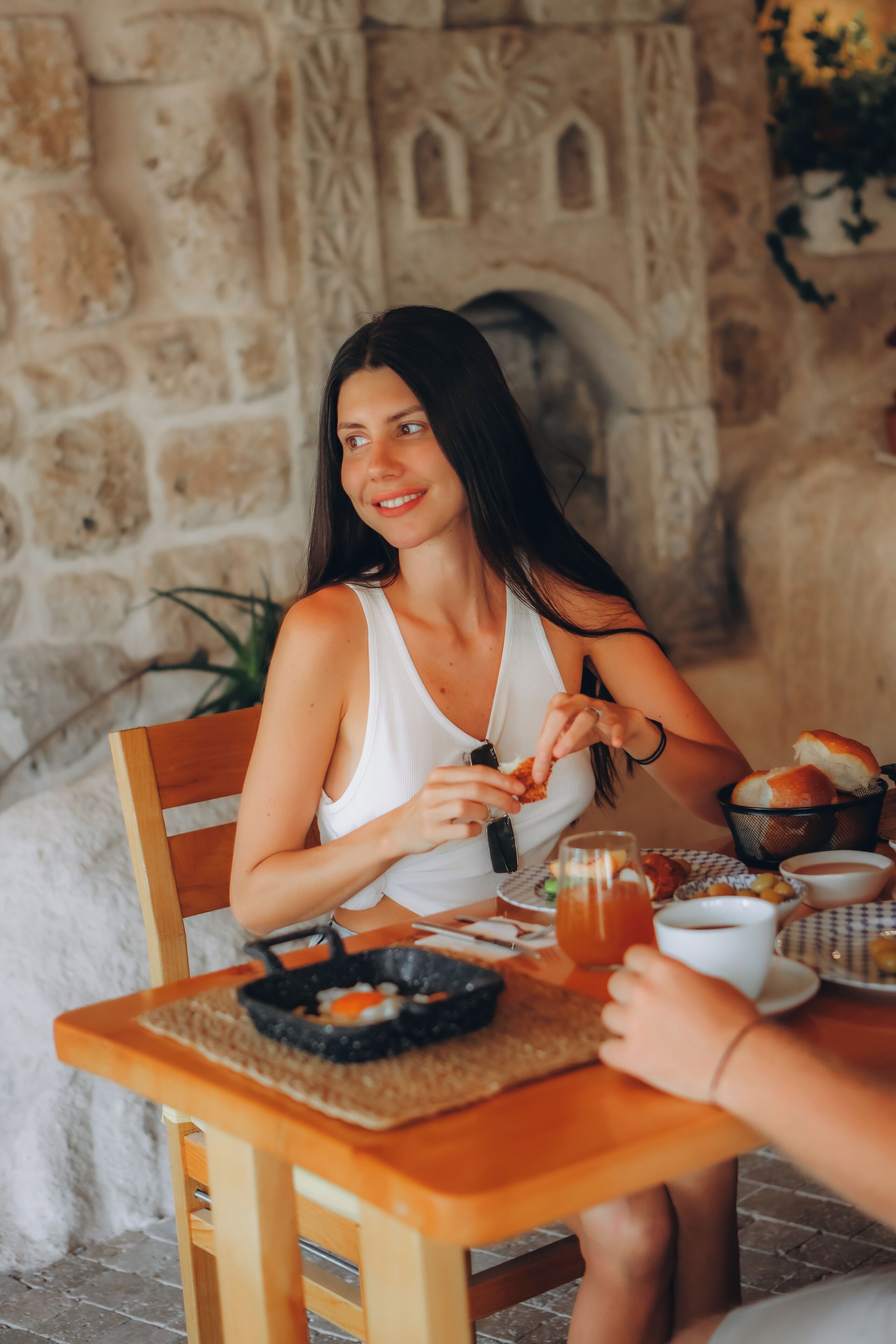 Una persona sentada a una mesa de madera con una cesta de pan, una taza de café y un plato de comida.