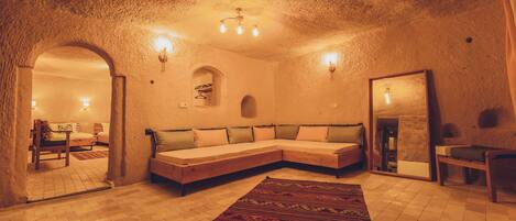 A cozy, well-lit room with a large sofa, a patterned rug, and a mirror reflecting the interior.