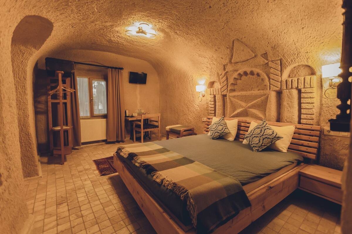 A cozy, stone-walled bedroom with a wooden bed, a small desk, and a television.