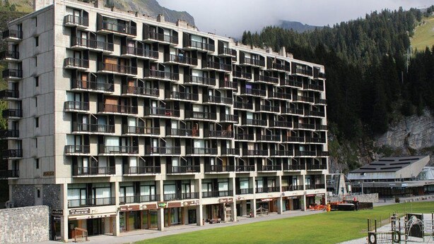 A multi-story hotel with a grid of balconies, a central courtyard, and a mountainous backdrop. - Ski-In/Ski-Out 3-Bedroom Apartment, Sleeps 8, Flaine Forum, Stunning Mountain View (Flaine)
