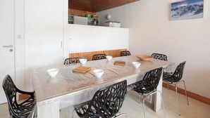 A dining area with a long table, black chairs, and a wooden ceiling. - Ski-In/Ski-Out 3-Bedroom Apartment, Sleeps 8, Flaine Forum, Stunning Mountain View (Flaine)