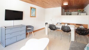 A modern living room with a wooden ceiling, a flat-screen TV, a dining area with a white table and black chairs, and a grey sofa. - Ski-In/Ski-Out 3-Bedroom Apartment, Sleeps 8, Flaine Forum, Stunning Mountain View (Flaine)