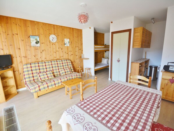 A cozy room with a plaid sofa, a wooden table, a bunk bed, and a kitchenette area.
