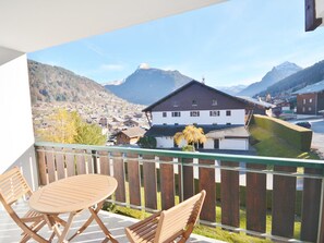 A balcony with a table and chairs, overlooking a mountain town with houses and a prominent mountain in the background.