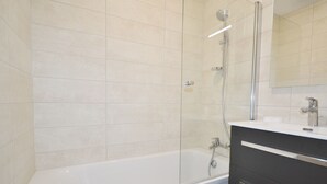 A modern bathroom with a glass-enclosed shower, a white bathtub, and a dark vanity with a mirror.