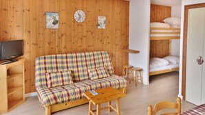 A cozy room with a plaid sofa, a wooden TV stand, a small table, a bunk bed, and a wall clock.