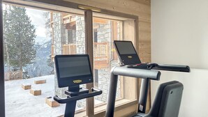 Un gimnasio con cintas de correr y una bicicleta estática, ventanas amplias y vistas a una montaña nevada.