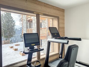 A gym with treadmills and a stationary bike, large windows, and a view of a snowy mountain. - Spacious apartment with WIFI, parking, spa and sports equipment (Montvalezan-La Rosière)