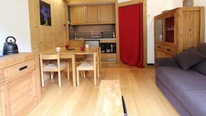 Un ambiente compatto con angolo cottura, mobili in legno, un divano e una tenda rossa.