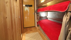 Una stanza angusta con letti a castello, pareti in legno, una porta con interruttore e un piccolo tappeto.