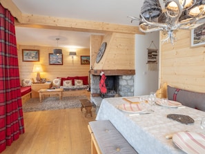Une pièce chaleureuse avec une cheminée en pierre, des murs en bois, une table à manger dressée avec des assiettes et des verres, et un banc.
