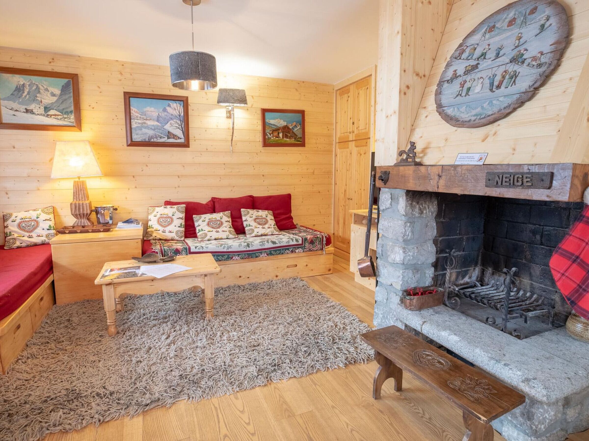 A cozy log cabin interior with a fireplace, wooden walls, and a sofa with red cushions.
