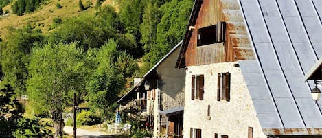 Un village de montagne pittoresque, avec des bâtiments en pierre, une route pavée et une végétation luxuriante.