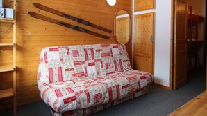 A cozy room with a wooden wall, a sofa with a patterned cover, a mirror, and a door leading to another room.