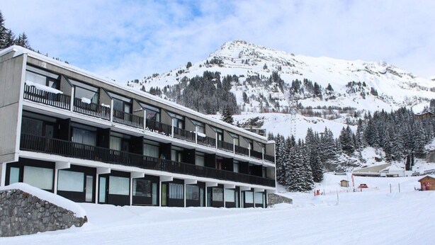 A modern multi-story hotel with balconies, set against a snowy mountain backdrop.