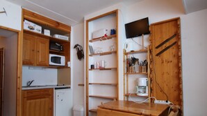 A compact kitchen with wooden cabinets, a microwave, a coffee maker, and a TV mounted on the wall.