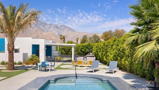 A modern outdoor pool area with a white building, seating, and a view of mountains. - Pickleball Court | Pool | Hot Tub (Palm Springs)
