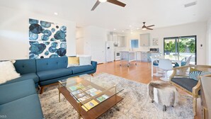 A modern living room with a blue sofa, a coffee table with magazines, and a large abstract painting on the wall. - Pickleball Court | Pool | Hot Tub (Palm Springs)