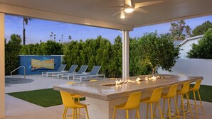 A covered outdoor area with a fire pit, bar stools, and lounge chairs. - Pickleball Court | Pool | Hot Tub (Palm Springs)