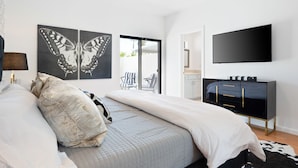 A modern bedroom with a bed, a ceiling fan, a flat-screen TV, and a black TV stand. - Pickleball Court | Pool | Hot Tub (Palm Springs)