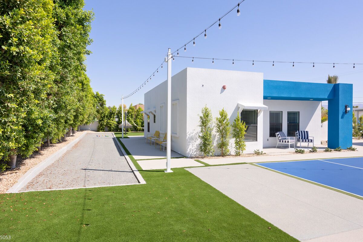 Un edificio moderno con fachada blanca y azul, un camino de entrada pavimentado y un césped bien cuidado.