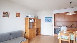 A compact living space with a sofa, wooden shelves, a dining table, and a kitchen area.